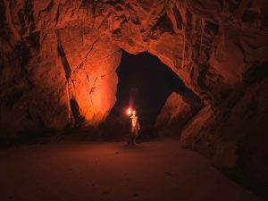 Person Standing and Holding Lamp Inside Cave