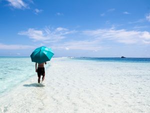Person Walking on Seashore Holding Blue Umbrella